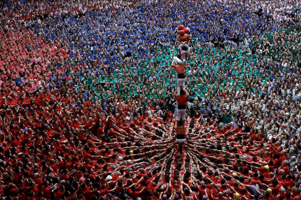 Multitud de personas apiñadas y abrazadas fuertemente formando la base circular de un castillo humano, todos vistiendo camisas del mismo color.