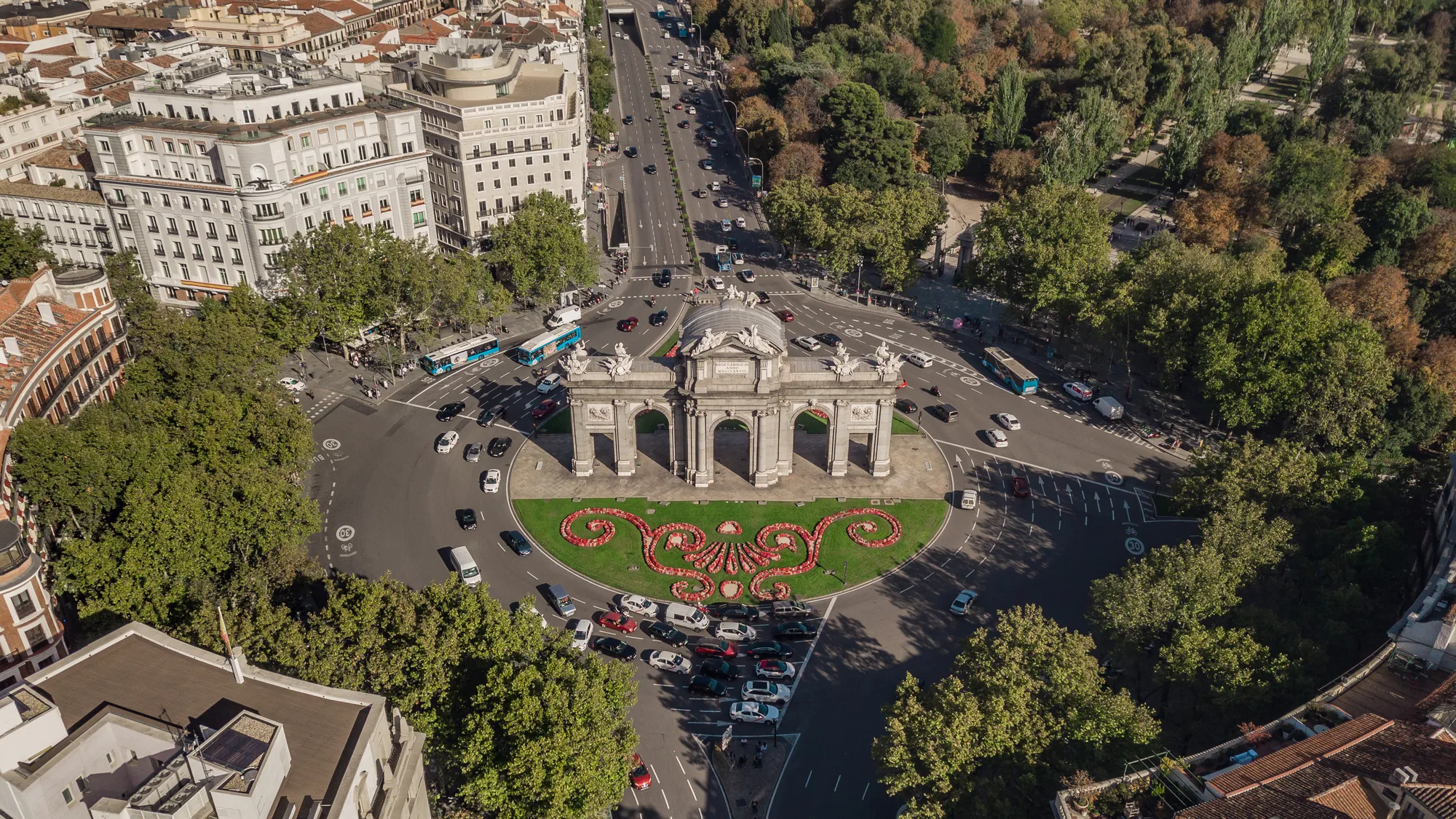 Vista de la Puerta de Alcalá rodeada de tráfico y turistas paseando en un día soleado de verano.
