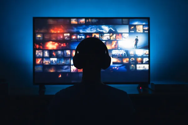 Persona sosteniendo un mando a distancia frente a un televisor que muestra el menú de una plataforma de streaming.